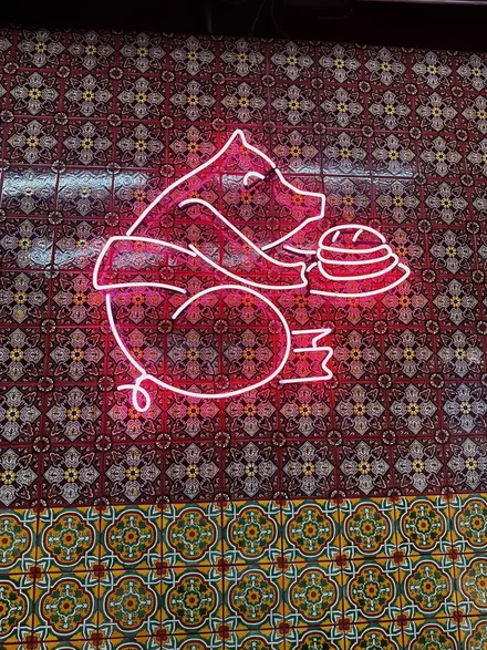 A pink neon sign of a pig carrying a torta on a patterned wall.