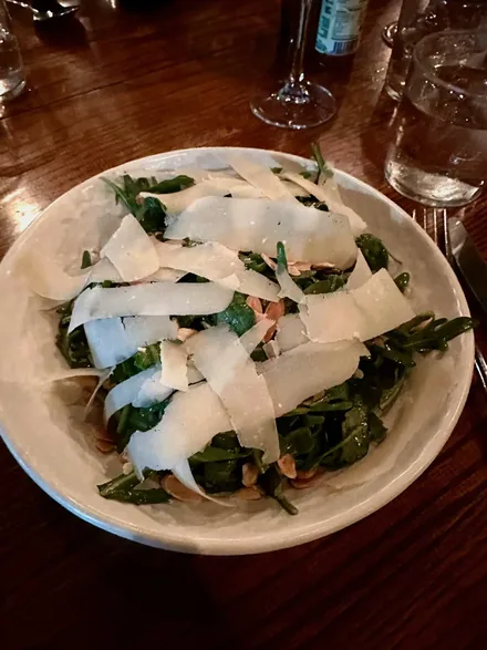 A circular white plate with arugula and large, wide shavings of Parmesan cheese